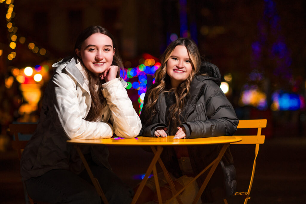 Night photos of two girls sitting at a table with holiday lights behind them