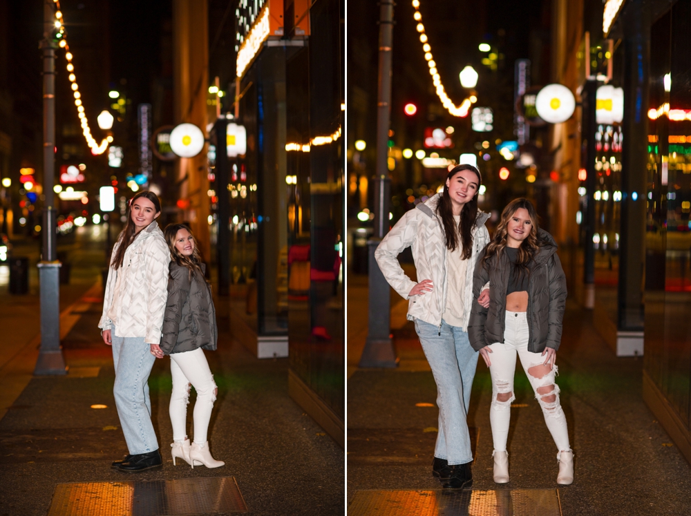 Two teen girls standing on a lighted downtown Pittsburgh sidewalk at night during the holidays.